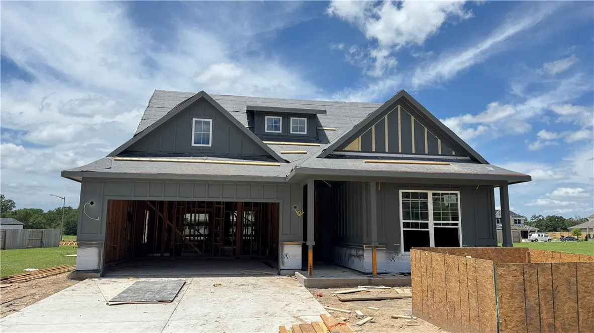 A new construction home with gray siding, a two-car garage, and a concrete driveway under a blue sky with white clouds.