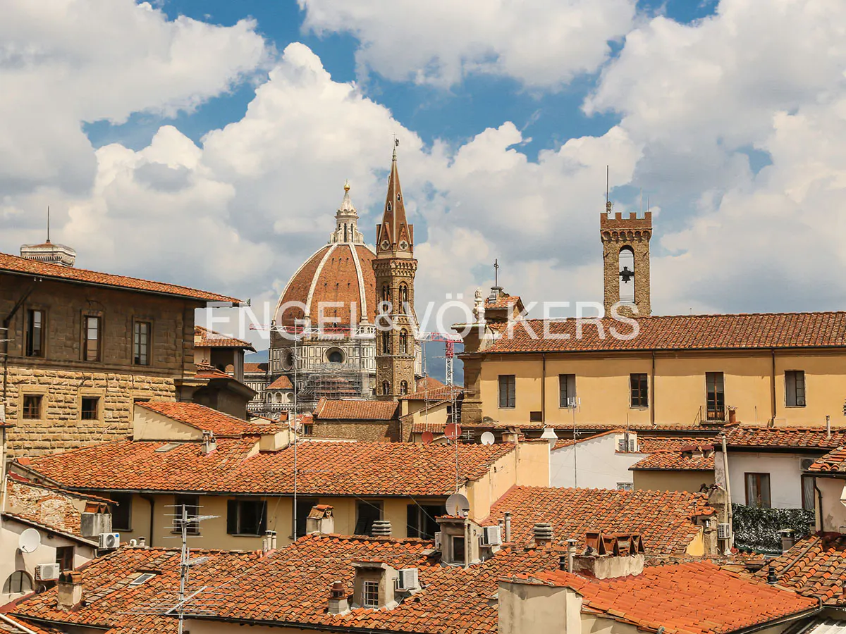 Florence cityscape featuring terracotta rooftops, the Duomo, and a bell tower under a blue sky with fluffy white clouds.