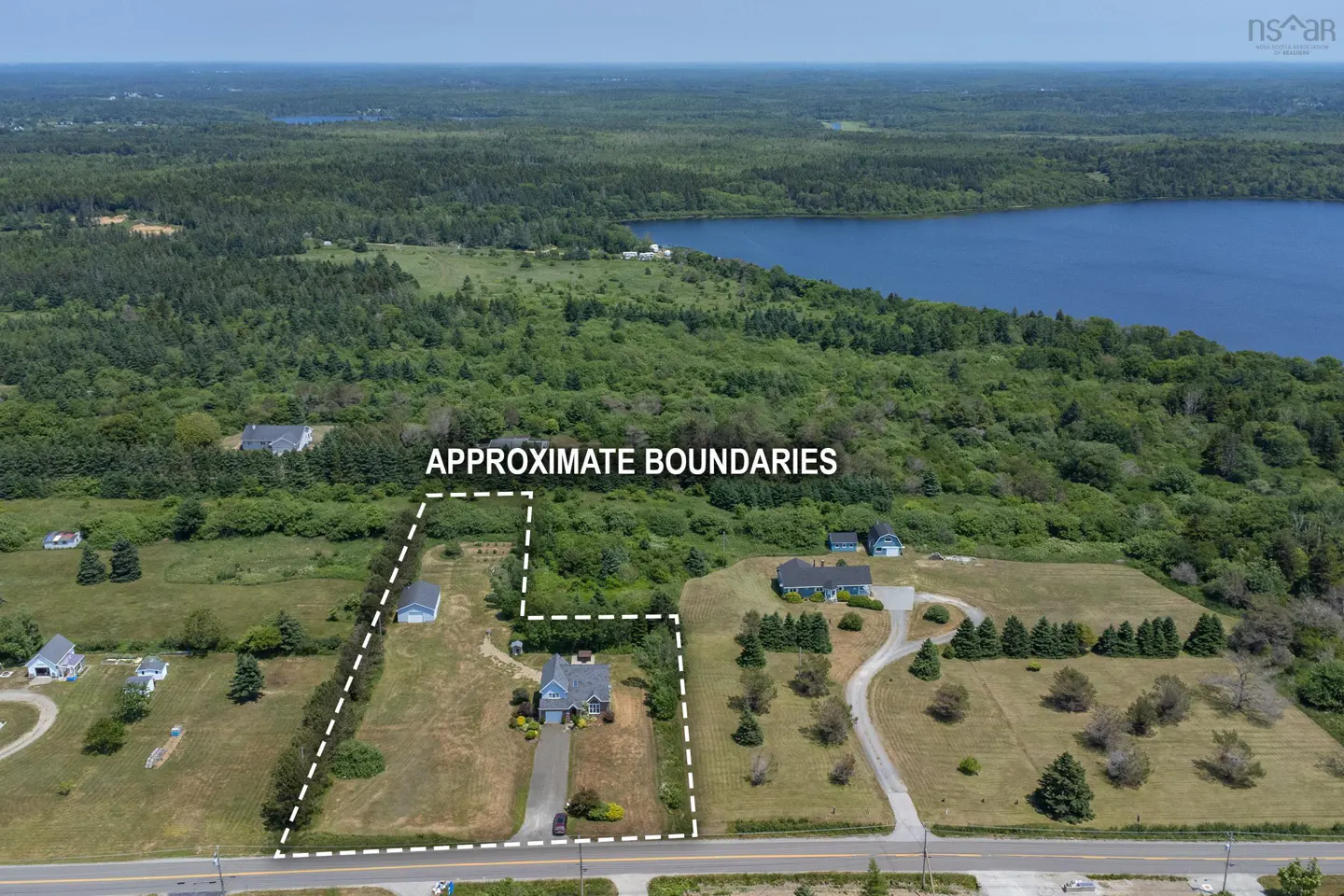 Aerial view of a property with approximate boundaries marked in white, near a lake and forest.