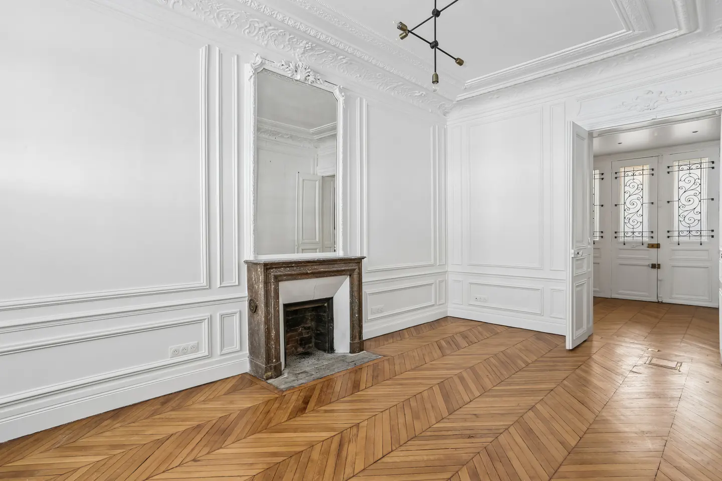 Bright room with white walls, ornate molding, a marble fireplace, a large mirror, and herringbone hardwood floors.