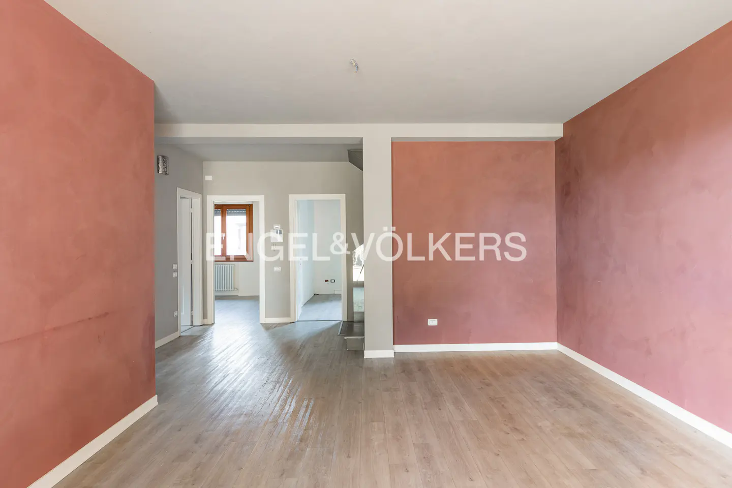 Empty room with pink walls and light wood floors. Doorways lead to other rooms. Engel & Völkers logo on the wall.