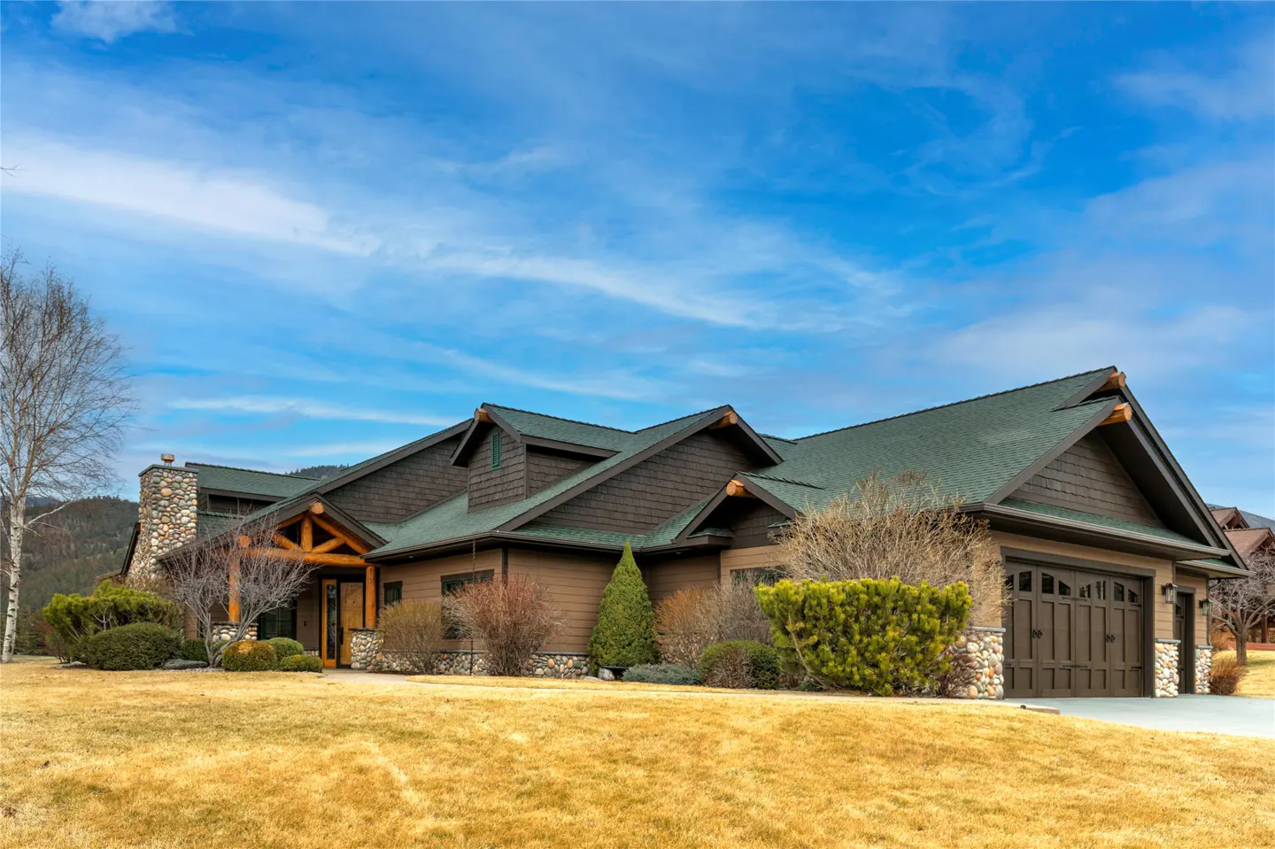 A brown house with a green roof and stone chimney sits on a golden lawn under a blue sky.