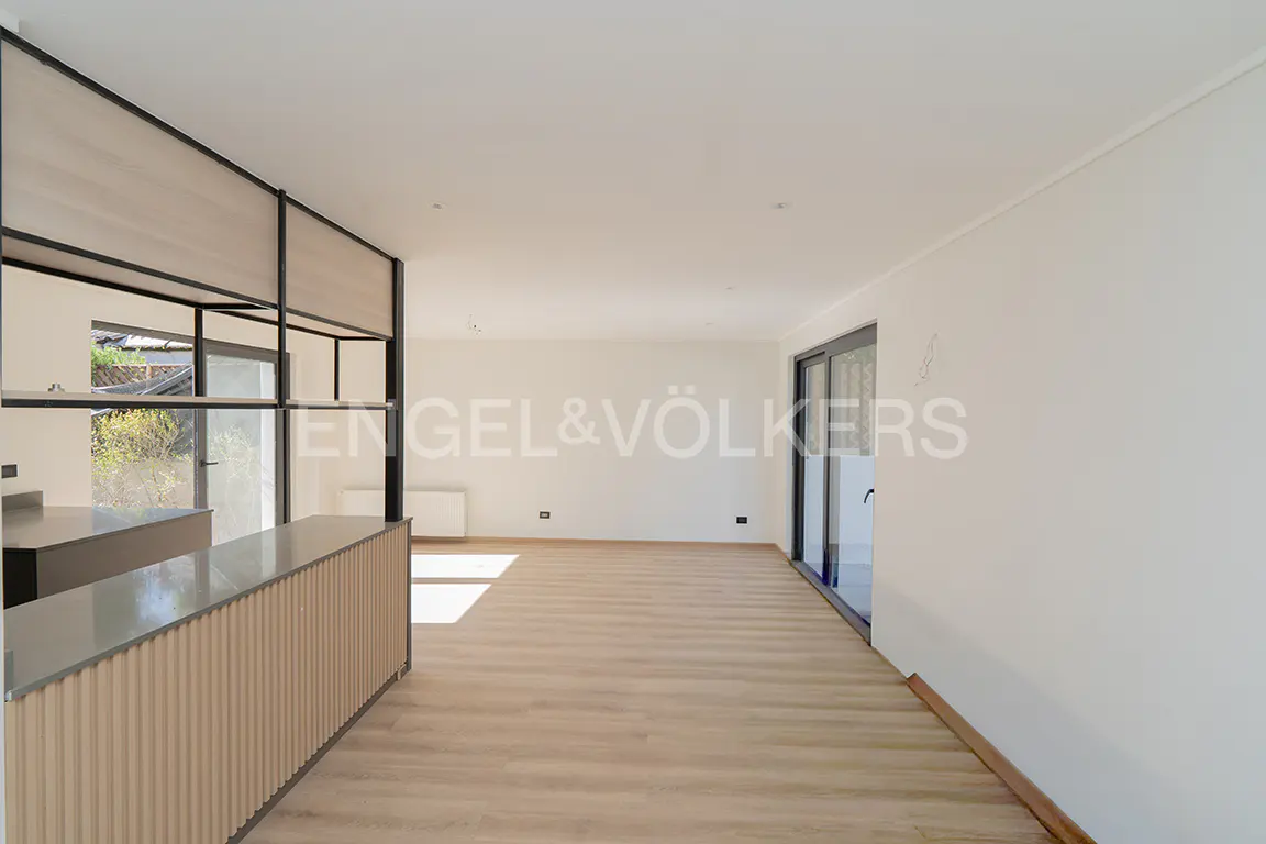 Bright, empty room with light wood floors and white walls. A kitchen island with a black frame is on the left. Sliding glass doors are on the right.