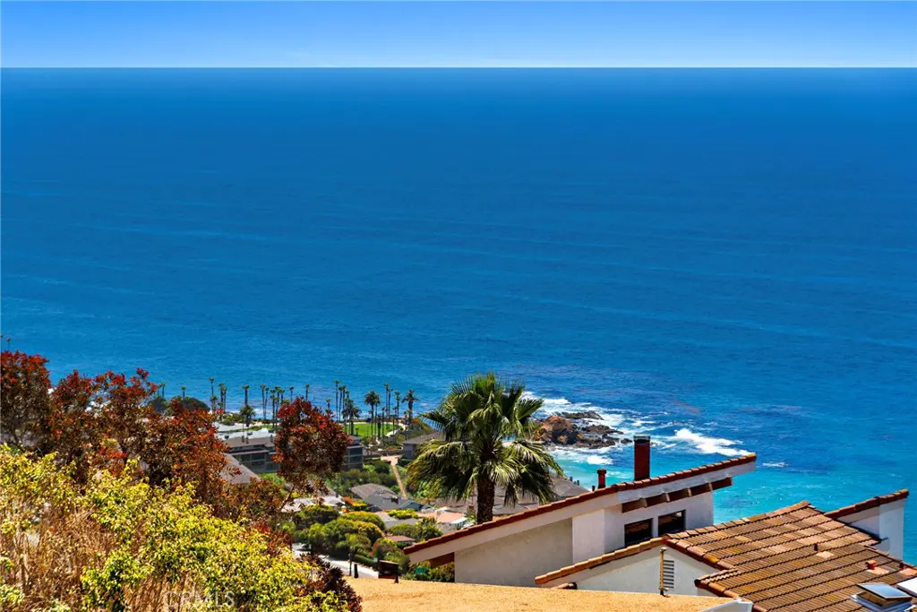 Ocean view from a hillside home with a red tile roof, palm trees, and blue water.