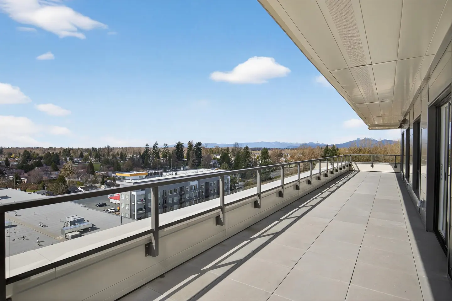 Spacious apartment balcony with tiled flooring, metal railing, and a panoramic view of the city and distant mountains.