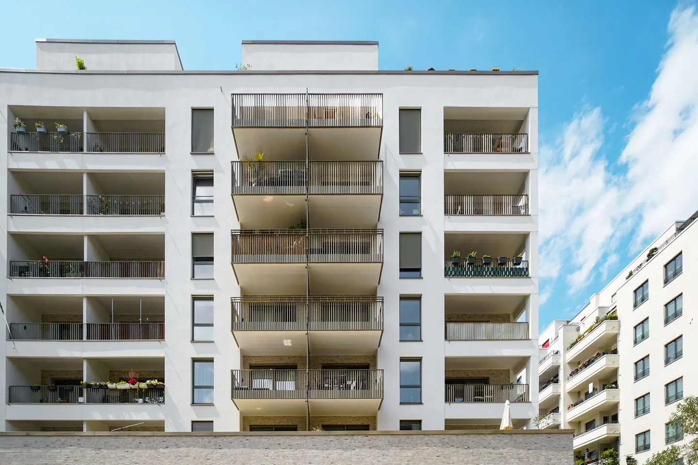 Exterior of a modern white apartment building with balconies and black railings against a blue sky.