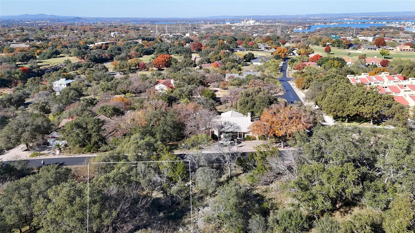 Aerial view of a wooded residential area with a vacant lot outlined in white, houses, and a distant lake.