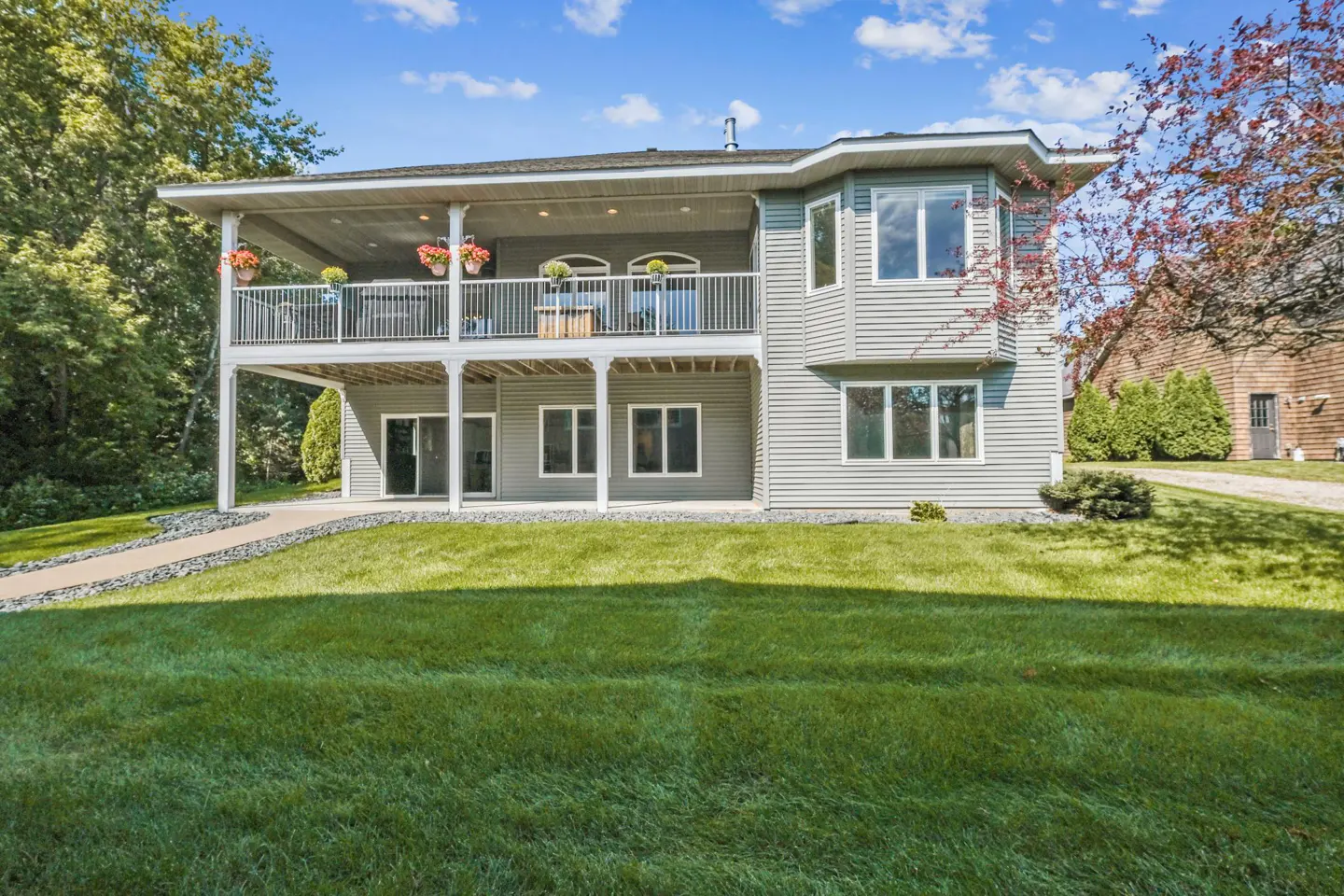 Two-story gray house with a white balcony and flower boxes overlooking a green lawn under a blue sky.