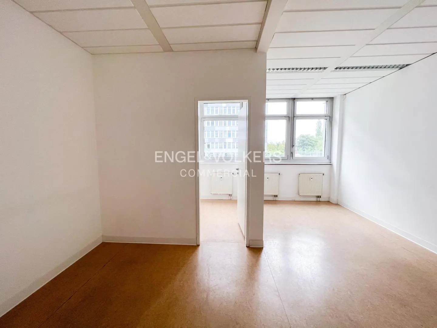 Empty office space with white walls, brown floor, and a window with a view of a building.
