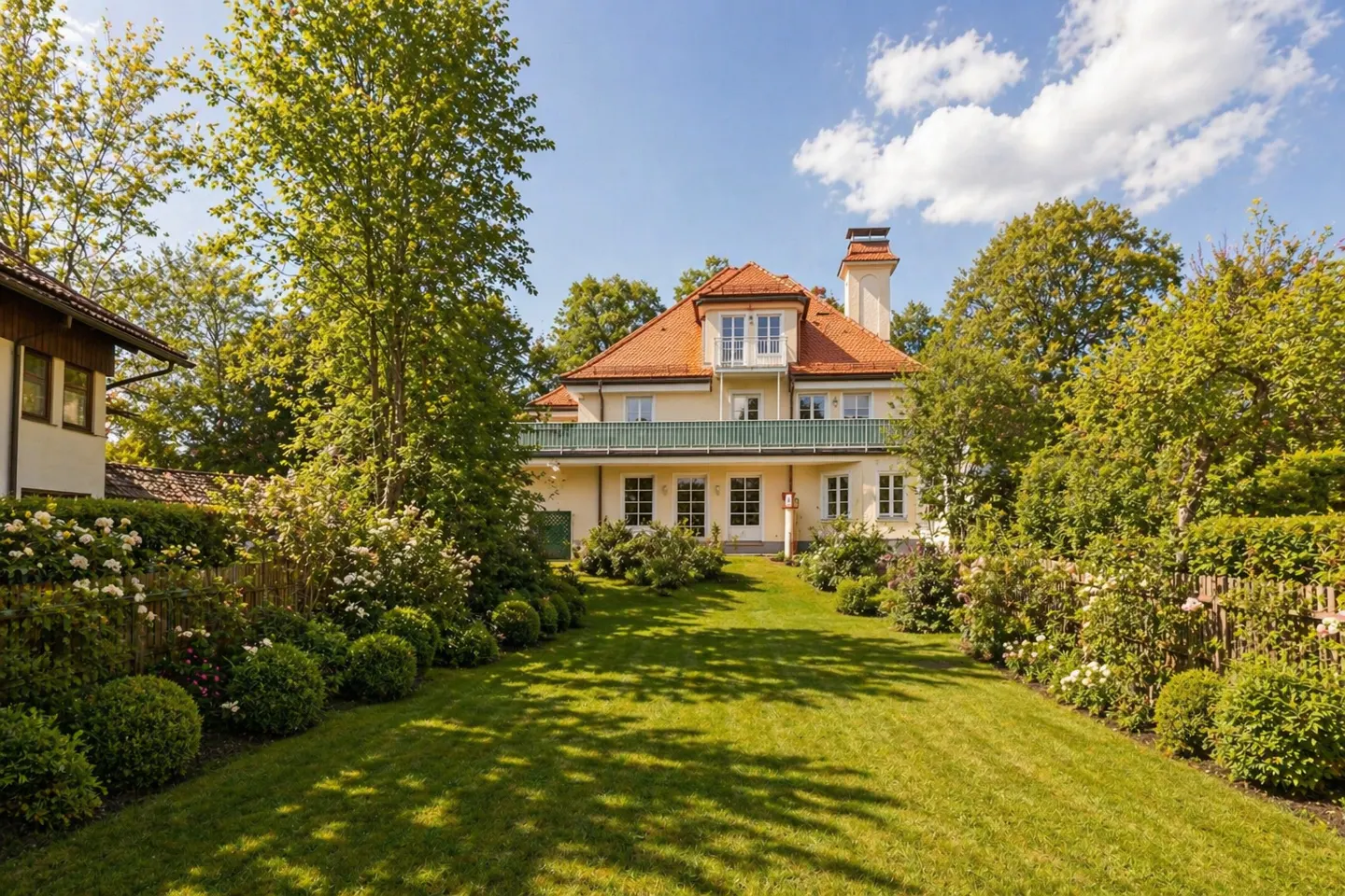 Two-story house with a red tile roof, cream-colored walls, green balcony, and a large green lawn.