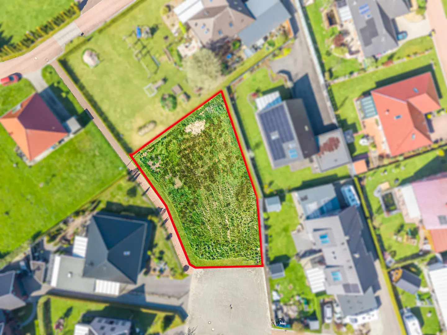 Aerial view of a vacant lot outlined in red, surrounded by houses and green lawns in a residential neighborhood.