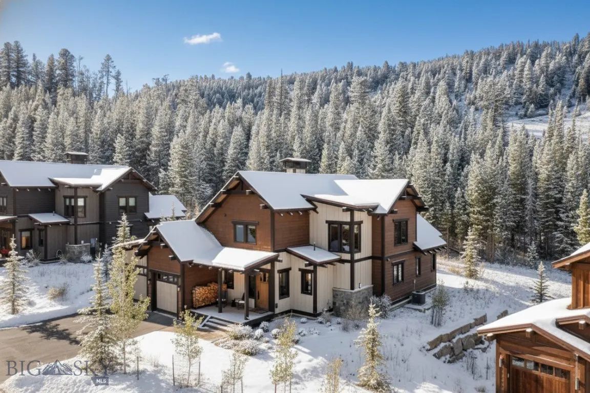 A two-story brown and white house with snow-covered roof, surrounded by snow-covered trees and a blue sky.
