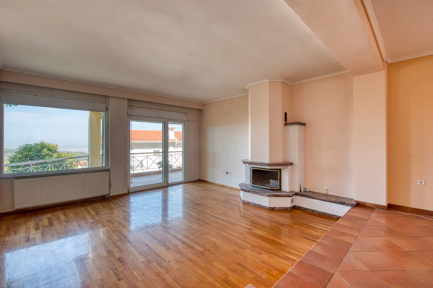 Bright living room with hardwood floors, a fireplace, and large windows with a view. Balcony access through sliding glass doors.