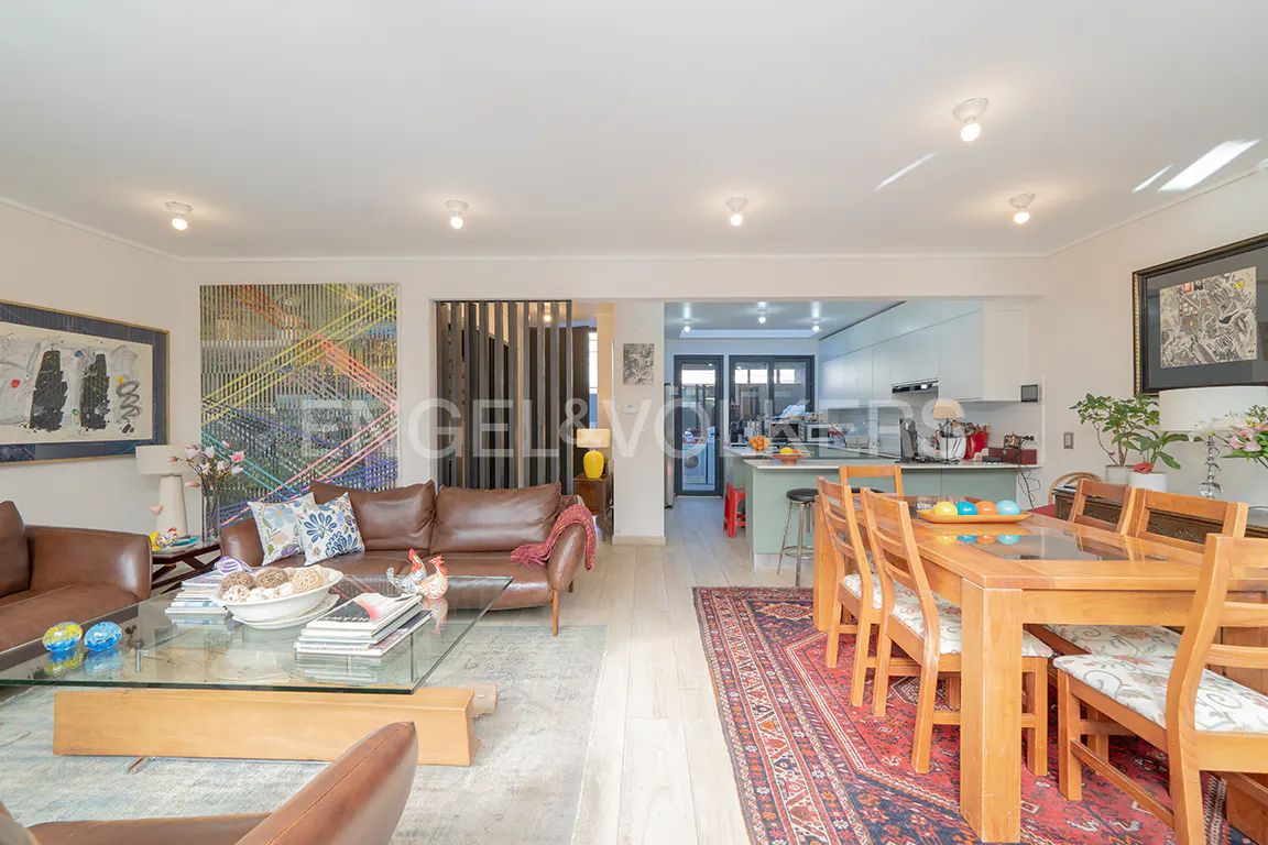 Open-concept living space with brown leather sofas, glass coffee table, and wooden dining table with chairs on a red patterned rug.