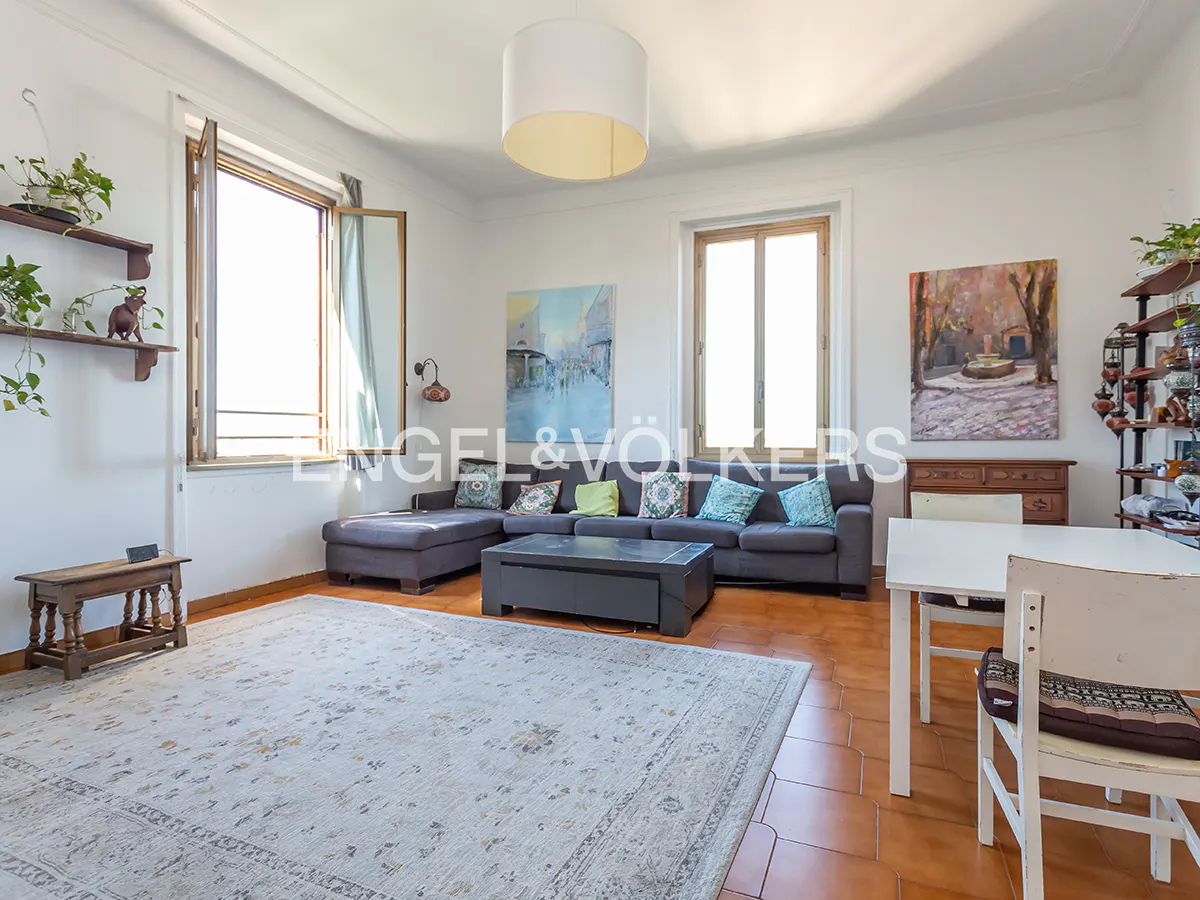 Bright living room with a grey sectional sofa, coffee table, large area rug, white walls, and terracotta tile floors.