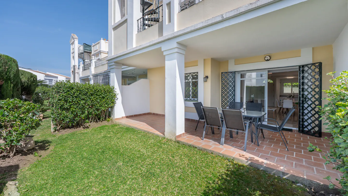 Outdoor patio with table and chairs on a brick patio, green grass, and a building with a spiral staircase.