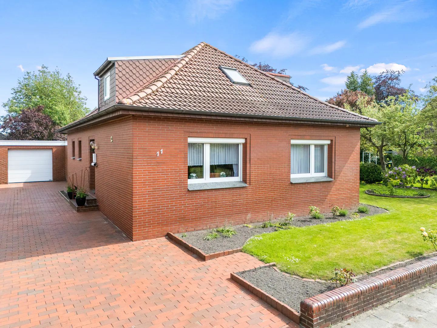 A red brick house with a tiled roof, white windows, a paved driveway, a garage, and a green lawn under a blue sky.