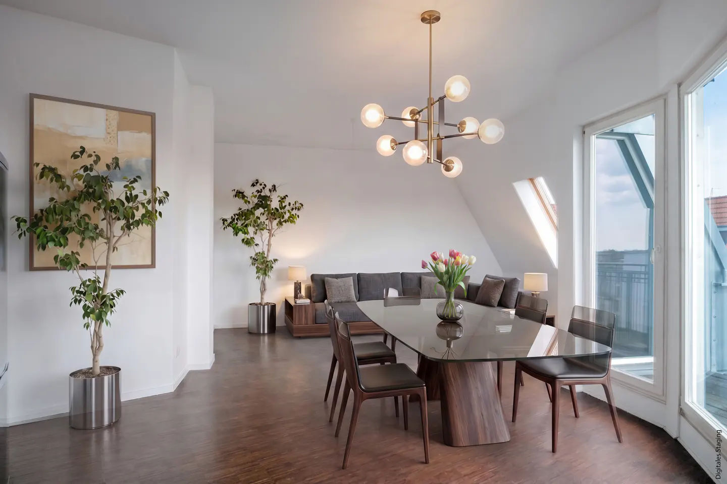 Modern dining area with a glass table, dark chairs, a brass chandelier, potted plants, and a sofa in the background.