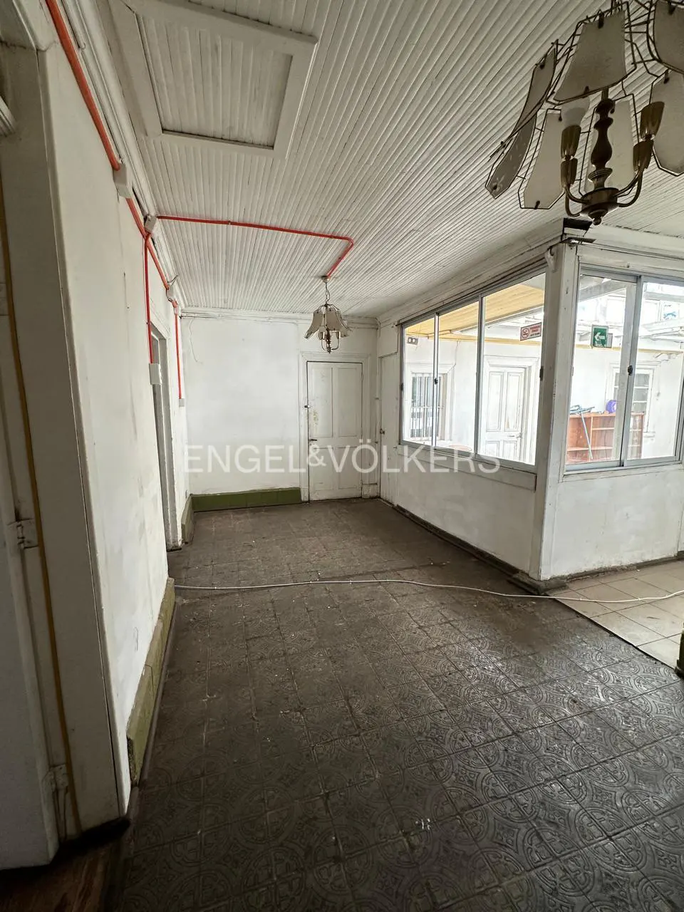 Empty room with white paneled ceiling, dark tiled floor, large windows, and exposed red electrical conduit on the wall.