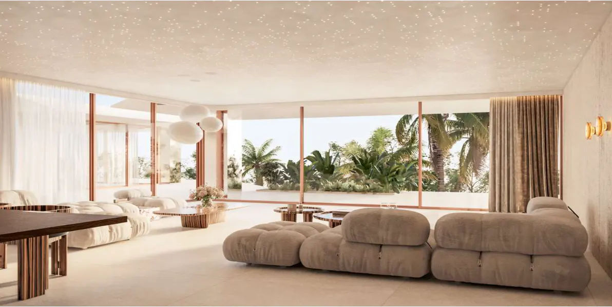 Bright living room with beige modular sofa, wood tables, and floor-to-ceiling windows overlooking lush tropical greenery.