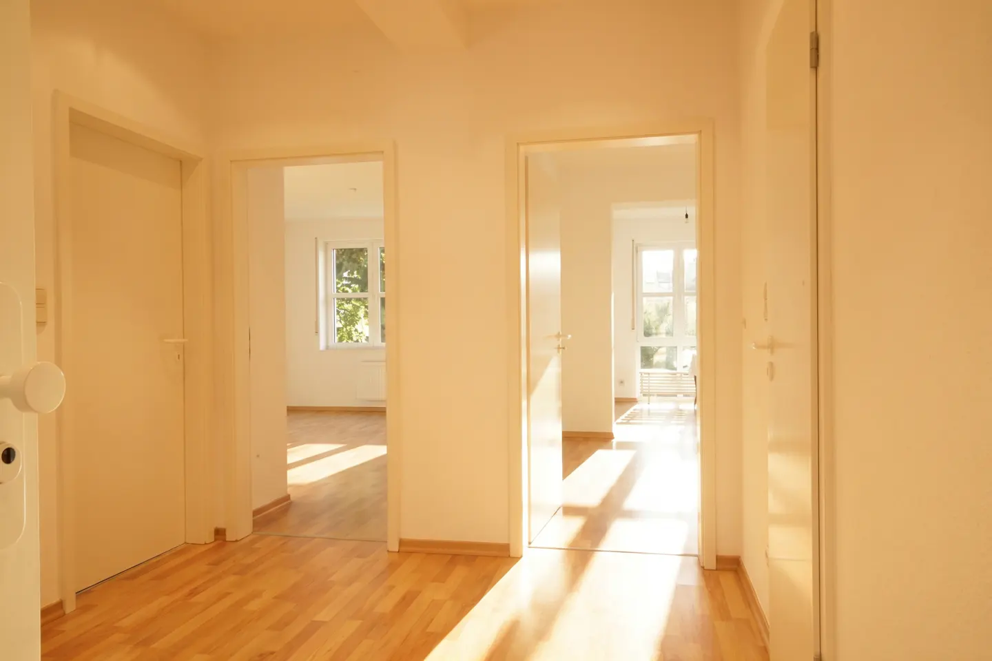 Bright hallway with light wood floors, white walls, and two open doorways leading to sunlit rooms with windows.