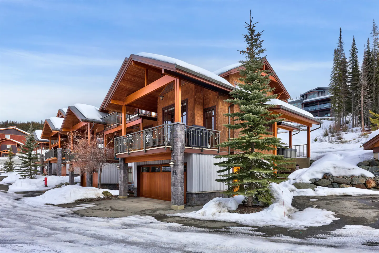 Exterior view of a brown, two-story house with a balcony and a garage in a snowy, mountainous area.