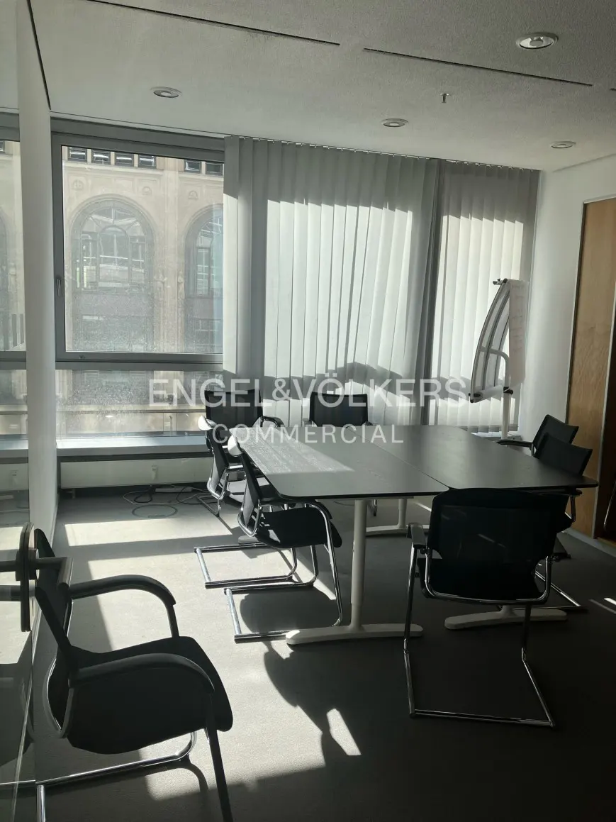Bright office space with a large table, black chairs, and a window with vertical blinds.