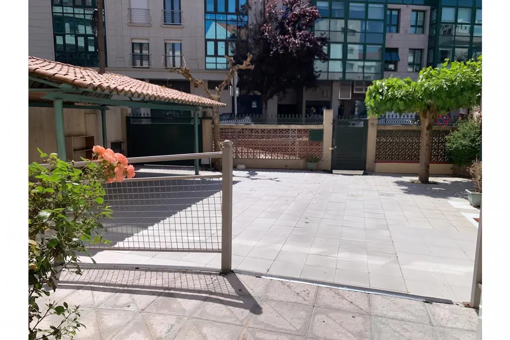 A courtyard with a tiled floor, a covered area with a red tile roof, and a metal fence. Trees and buildings are in the background.