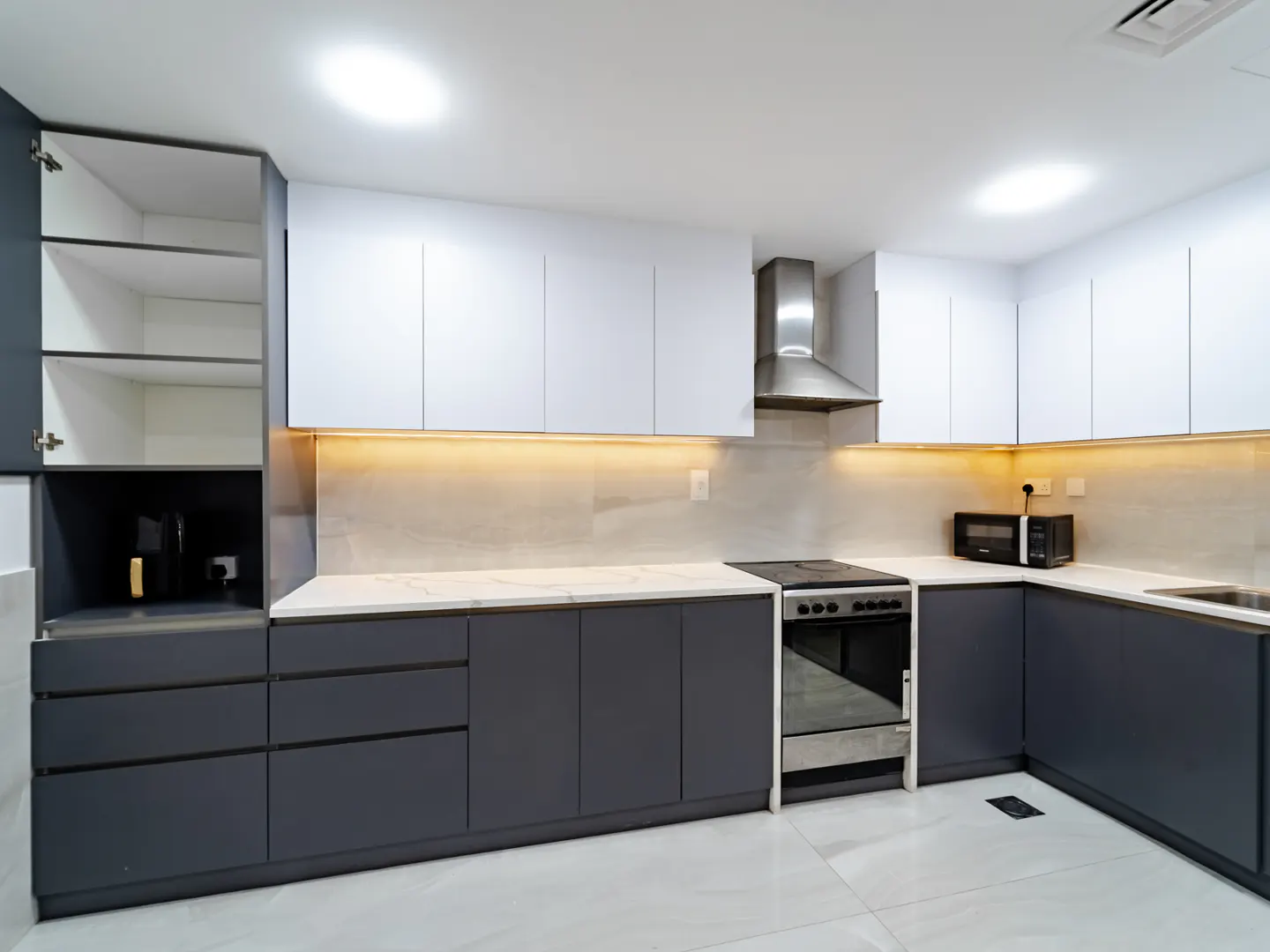 A modern kitchen with gray lower cabinets, white upper cabinets, and stainless steel appliances.