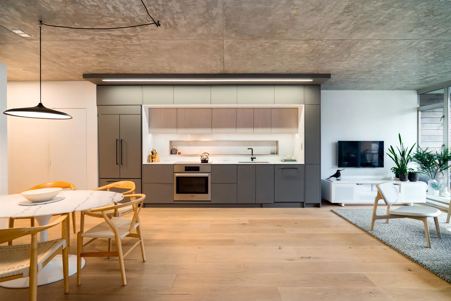 A modern open-concept kitchen and living area with gray cabinets, wood floors, and a marble dining table.
