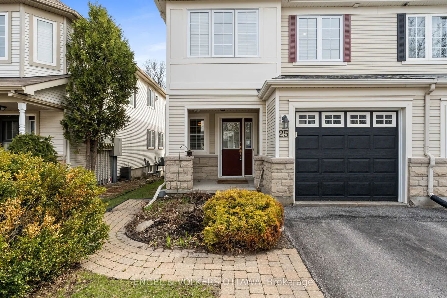 Beige two-story townhouse with a black garage door, brown front door, and brick walkway.