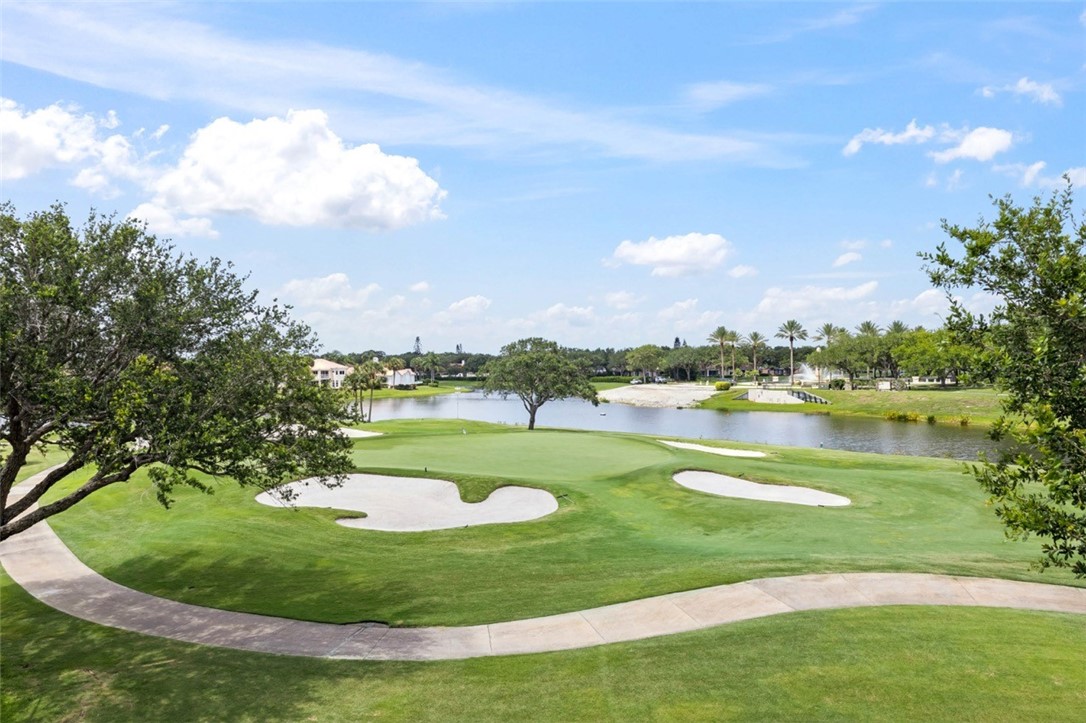 A scenic view of a lush green golf course with sand bunkers, a pond, and palm trees under a bright blue sky.