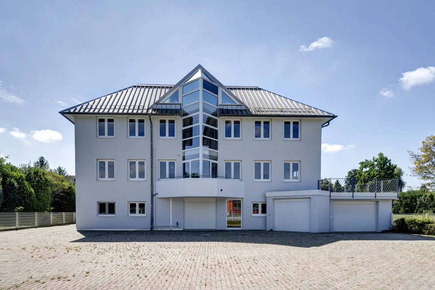 Two-story gray house with a glass tower, metal roof, and white trim under a blue sky.