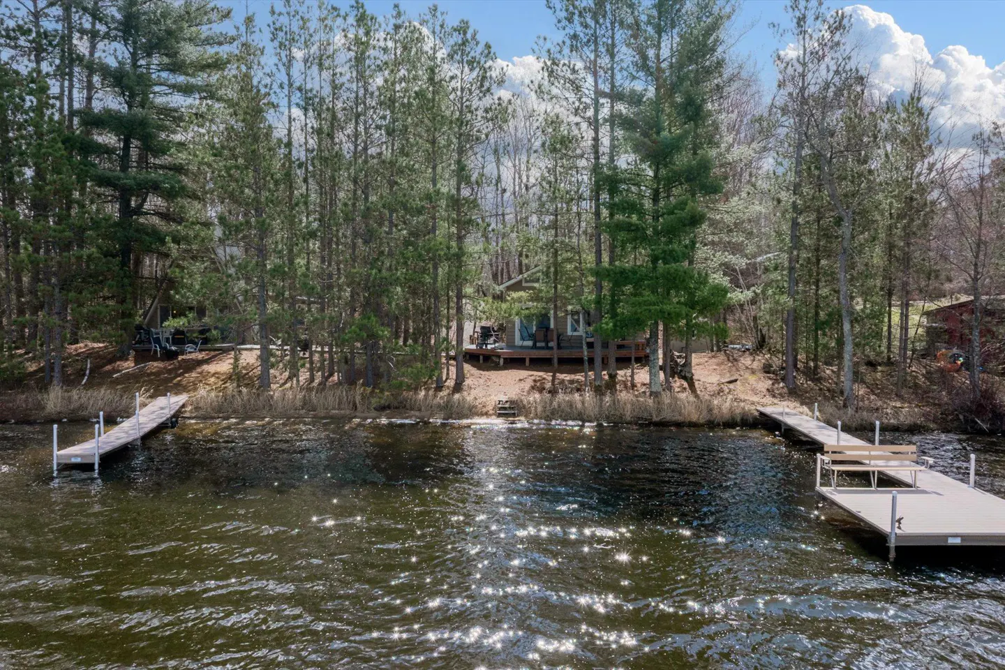 Lakefront property with two docks. A small house is nestled among tall trees on a sunny day.