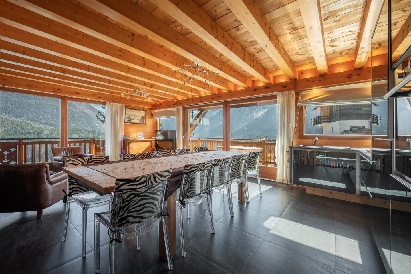 A bright dining room with a long table and zebra-print chairs. The room has wood paneling and large windows with mountain views.