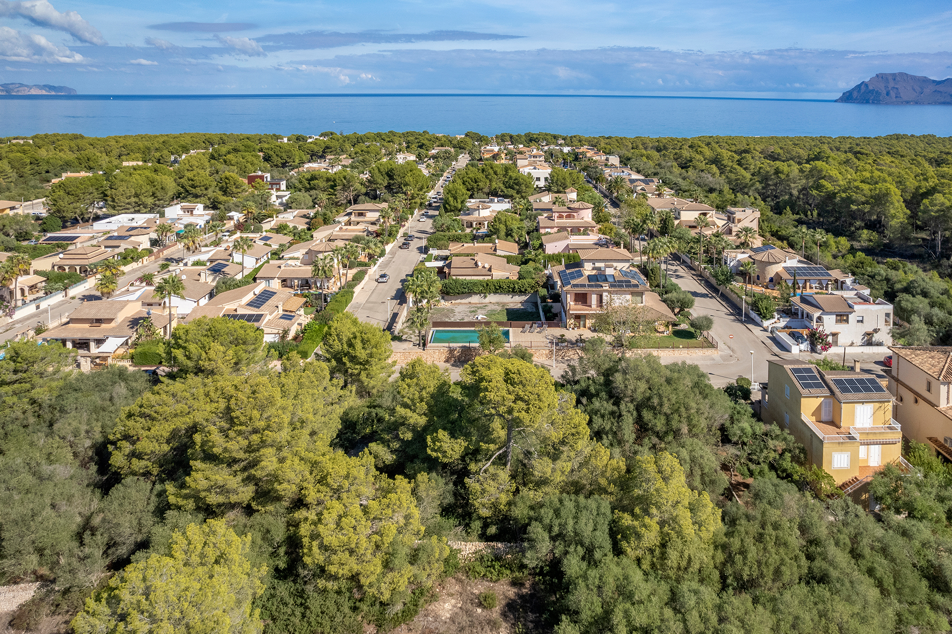 Aerial view of a coastal neighborhood with villas, lush green trees, and a swimming pool, overlooking the blue Mediterranean. [AI-generated text]