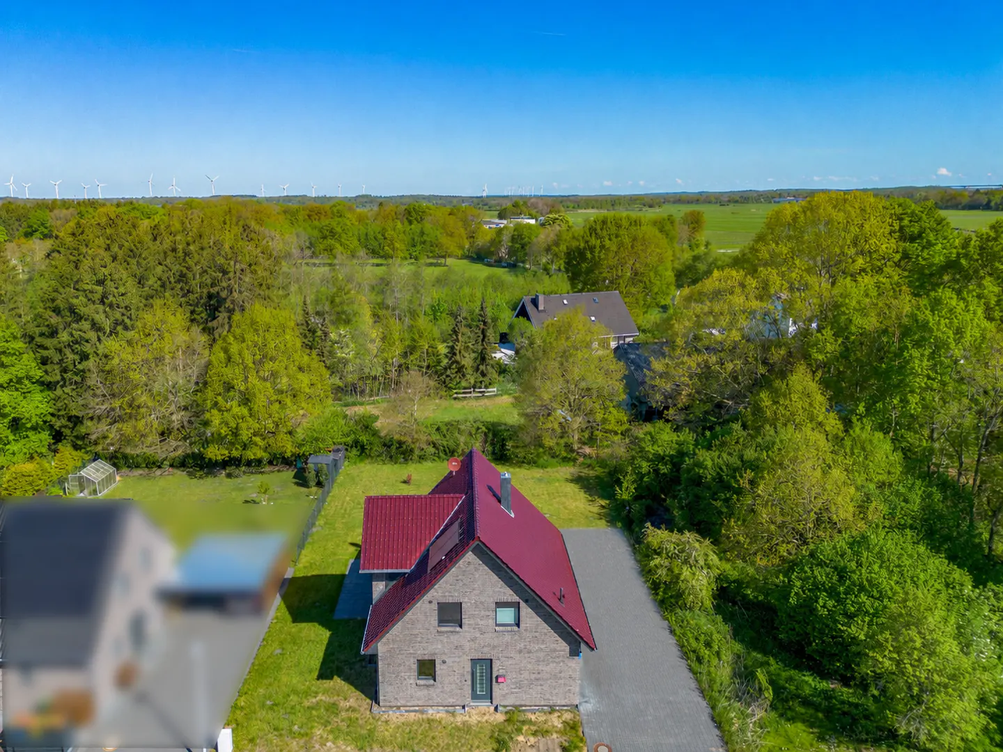 Aerial view of a gray brick house with a red roof, surrounded by green trees and a blue sky.