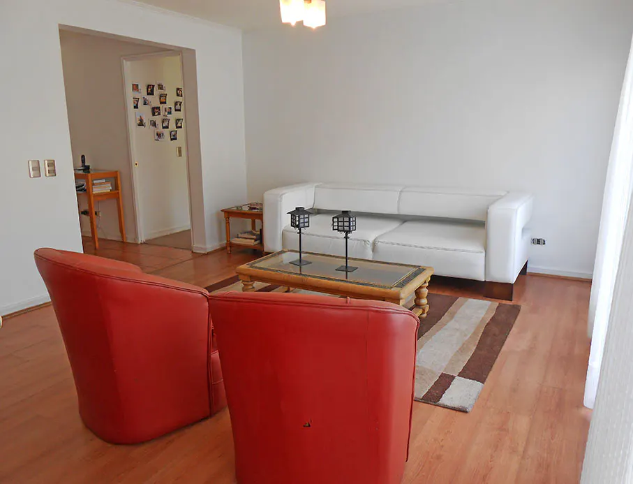Living room with two red chairs, a white sofa, and a glass-topped coffee table on a brown and beige rug.