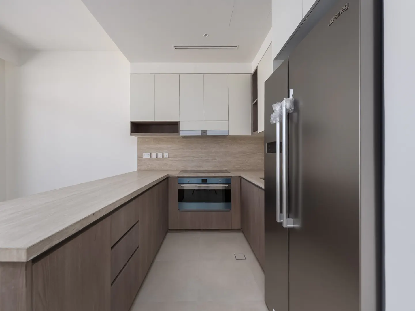 A modern kitchen with light wood cabinets, stone countertops, and a stainless steel refrigerator.