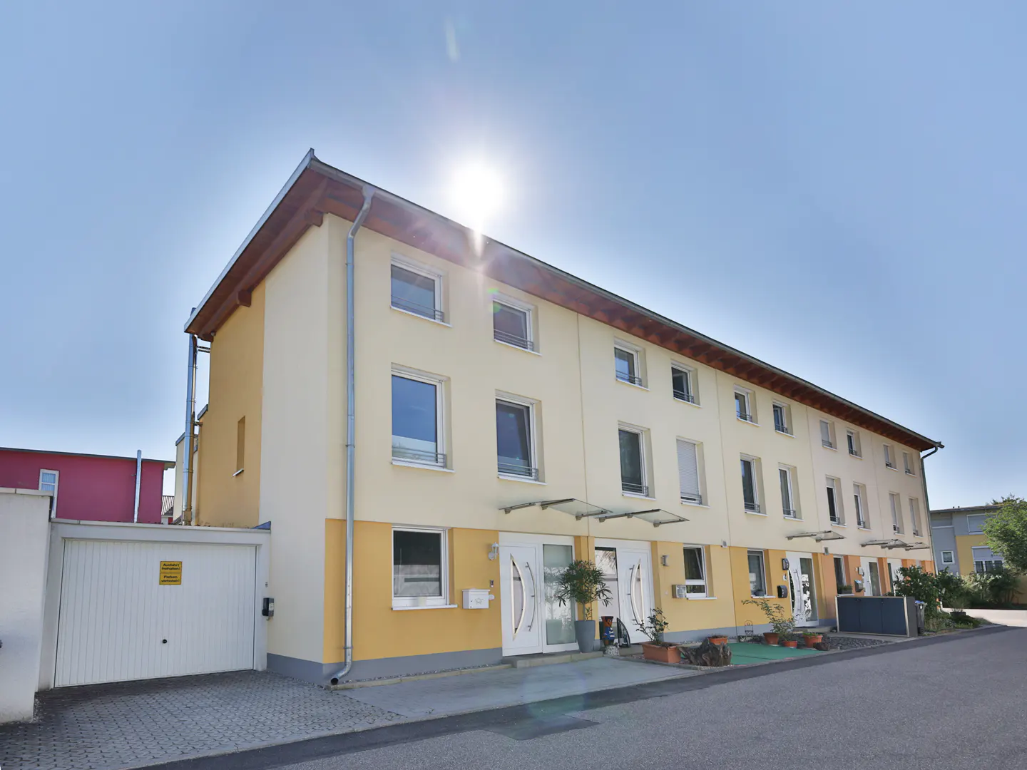 Row of attached two-story townhouses with yellow and cream facade, white doors, and a clear blue sky.