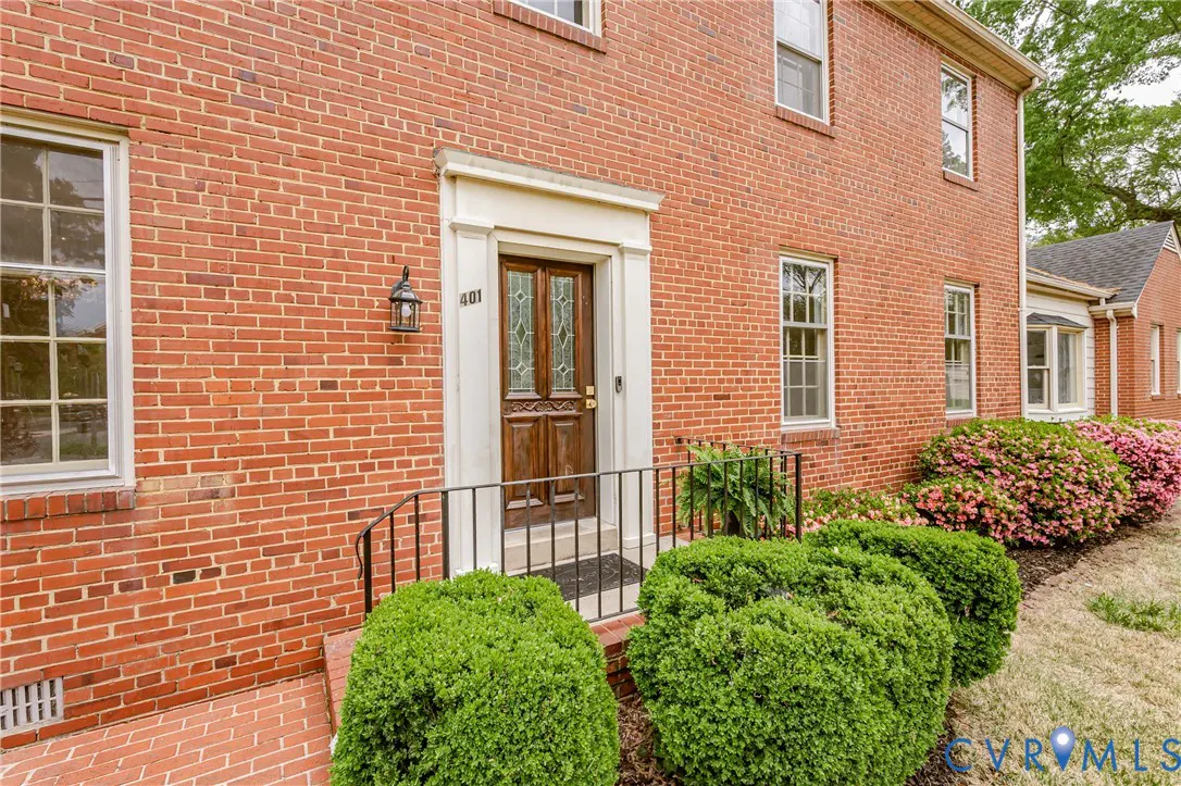 Red brick house exterior with a dark wood front door, white trim, and green bushes.