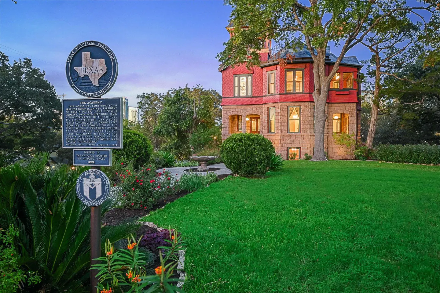 Exterior view of The Academy, a historic red and stone building with a green lawn and historical markers.
