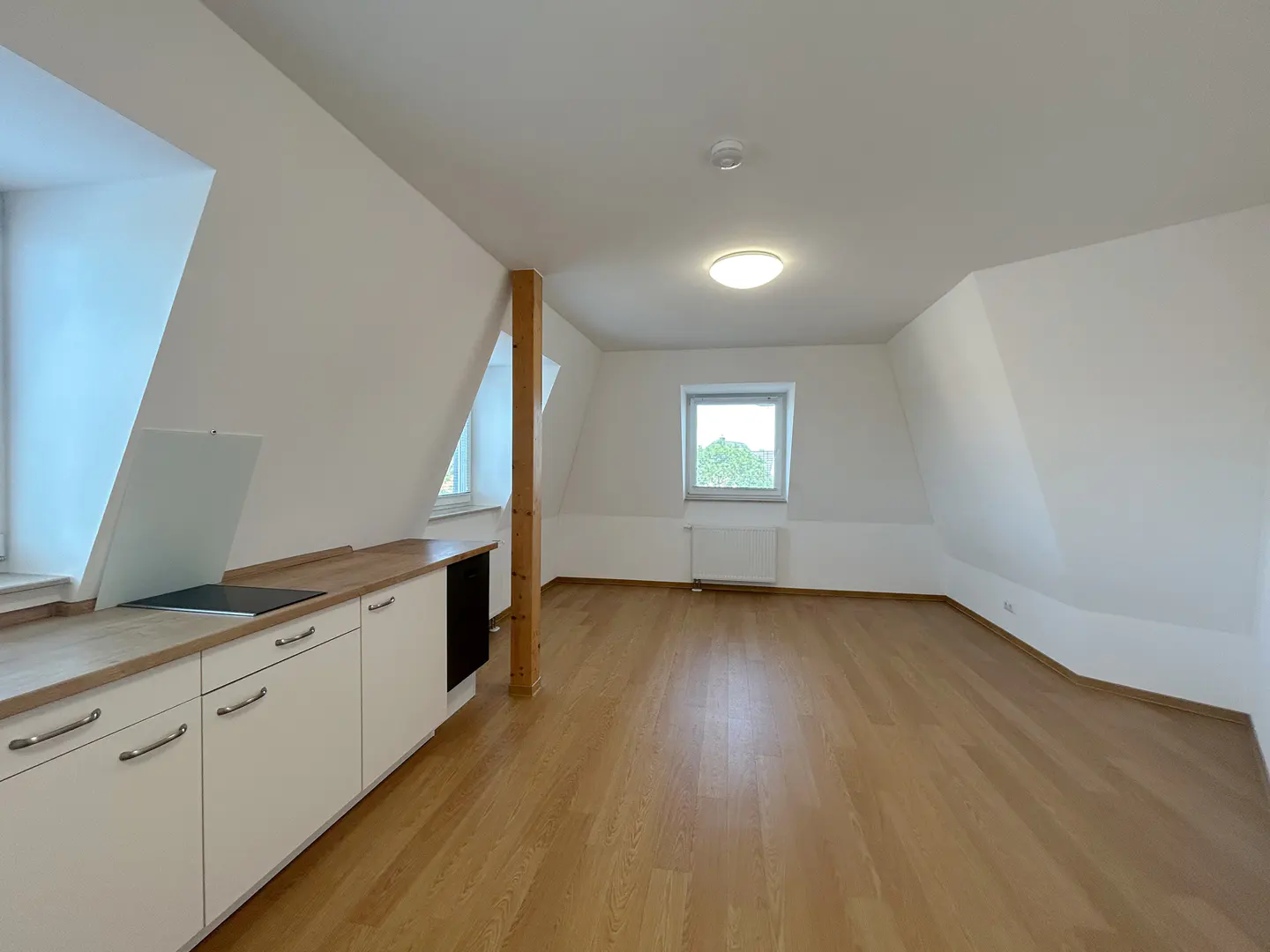 Attic apartment with white walls, wood floors, and a small kitchen area with white cabinets and a wood countertop.
