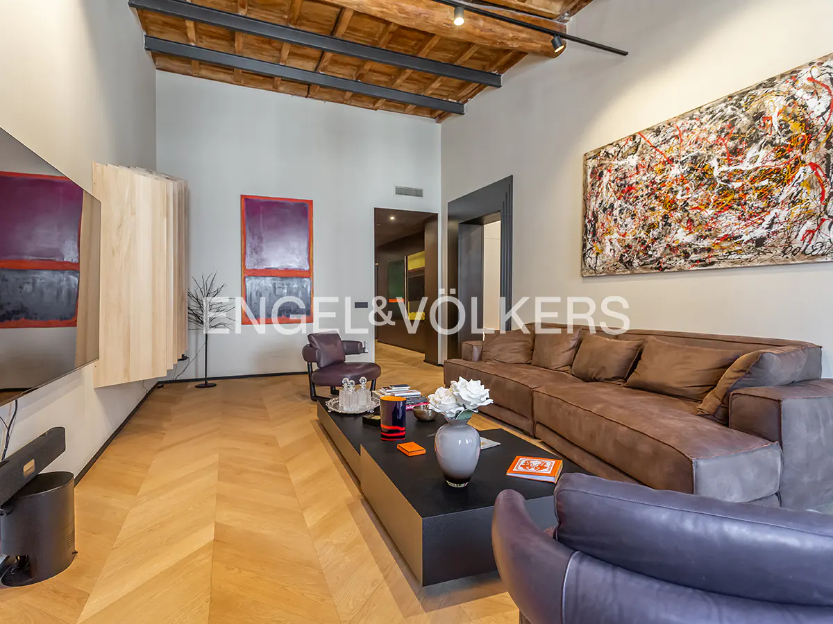 Modern living room with brown sofa, black coffee table, abstract art, and wooden ceiling beams over herringbone floors.