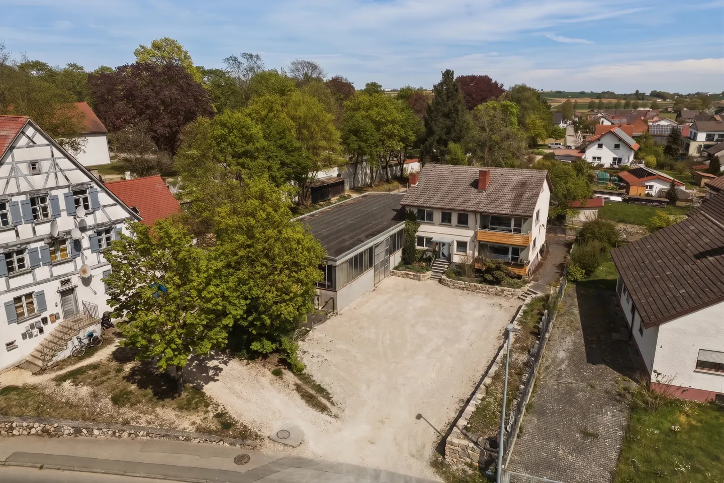 Aerial view of a property featuring a traditional timber-framed house, a flat-roofed workshop, and a gravel courtyard.