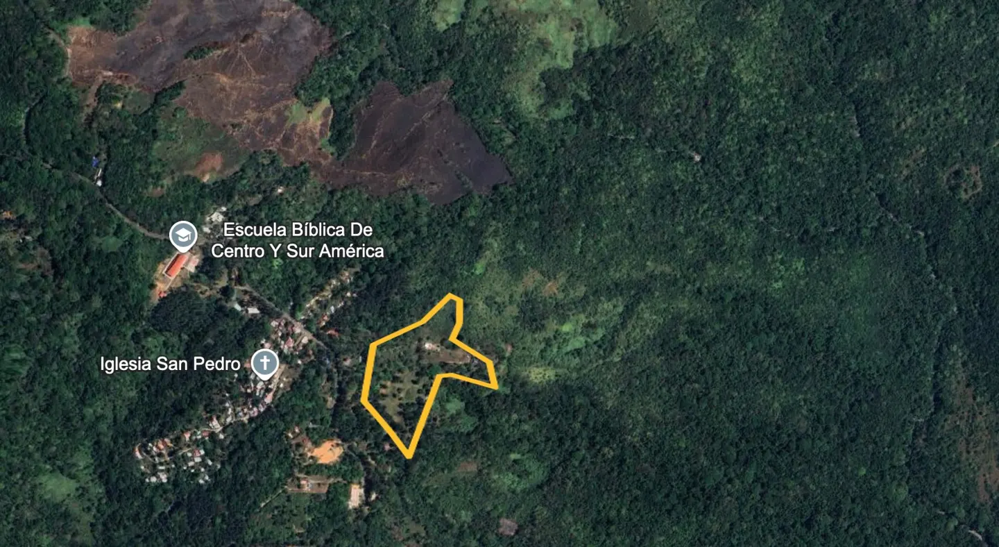 Aerial view of a property outlined in yellow, near a town with a church and school, surrounded by lush green forest.