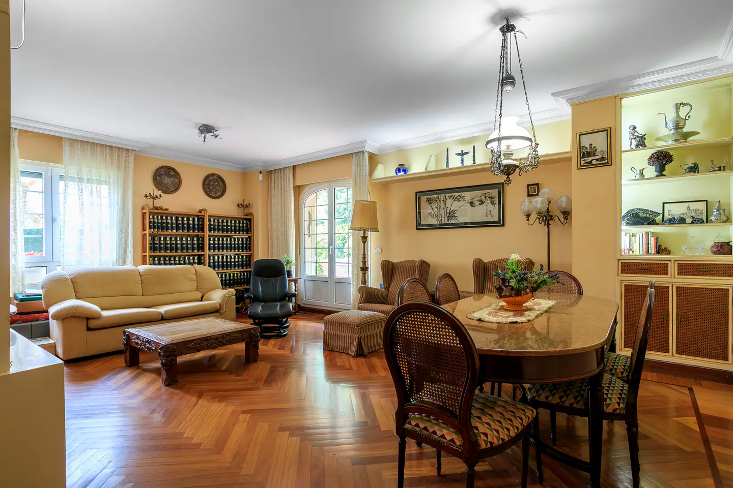 A living and dining room with parquet floors, a beige sofa, and a wooden dining table with chairs.