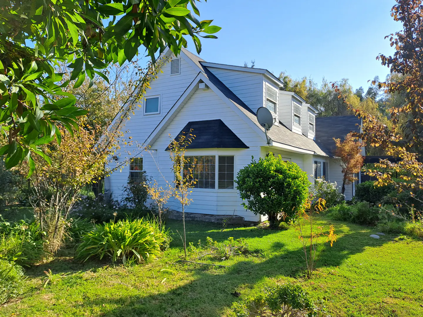 Exterior view of a two-story white house with a black roof, green lawn, and trees.