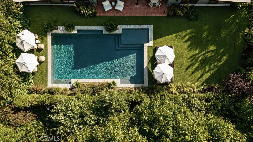 Aerial view of a backyard with a blue swimming pool, green lawn, white umbrellas, and lush green trees.