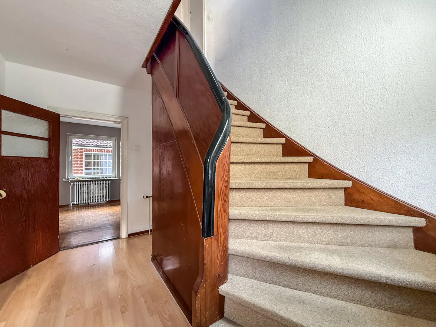 Interior view of a home's entryway with a carpeted staircase and an open wooden door leading to another room.